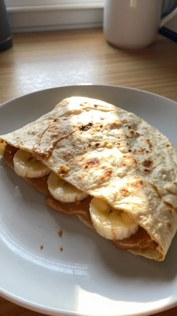 A real, authentic photo of a peanut butter banana sunrise quesadilla served on a simple plate, cut in half to reveal gooey peanut butter and soft banana inside a warm tortilla. The scene is captured with natural window light, casual and imperfect: a slightly tilted horizon, gentle overexposure on the tortilla edges, and a tiny lens flare from the sun. A few crumbs and a smear of peanut butter on the plate add realism. The background is a cozy kitchen counter with a hint of wooden texture, a coffee mug in the corner, and a faint, warm color cast. The image should look like it was shot quickly, no staging, with no text on the image. Include subtle camera imperfections: slight motion blur in the plate’s edge from a casual hand movement, a fingerprint on the lens, and grain that varies with the light. The final result should resemble an everyday iPhone photo, compressed to 1080p quality, with a slightly imperfect, natural feel and no AI-detection-friendly enhancements. Optional subtle post-processing hints: minimal color tweak, no heavy sharpening, a light fade to resemble a quick snap. No words or captions in the image.