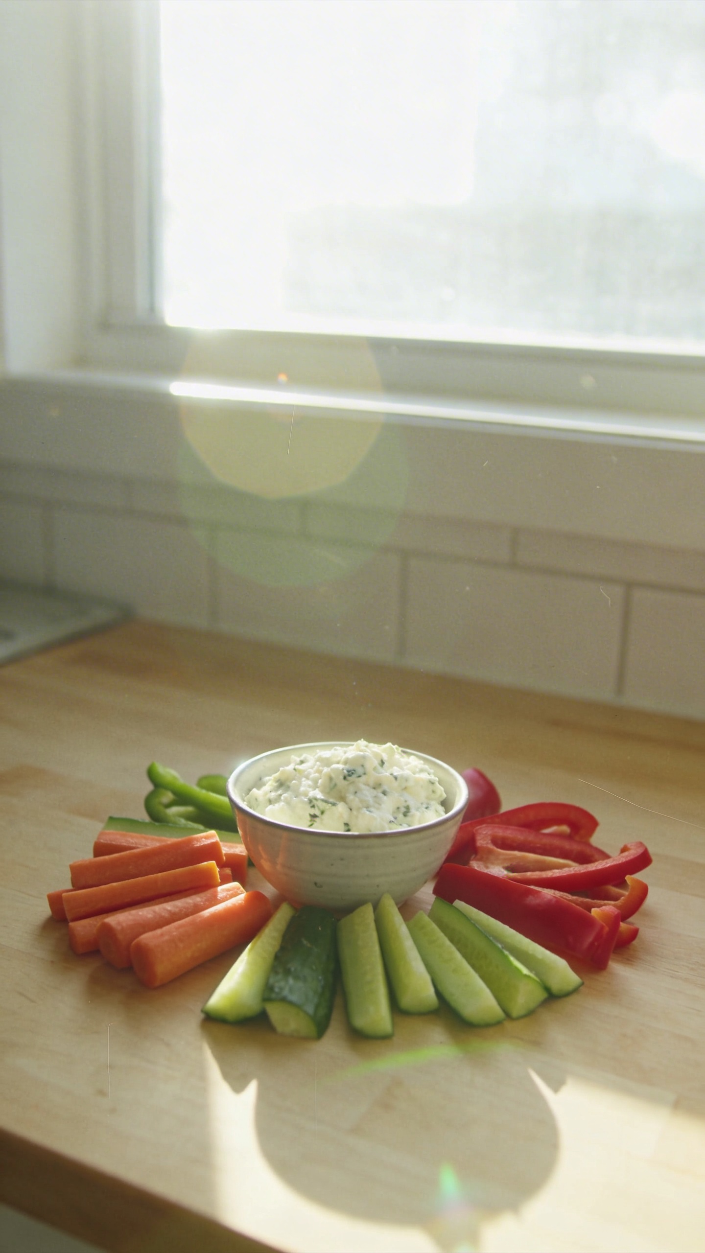 A candid, real-photo style image of a creamy herb cottage cheese dip with veggie sticks as the main subject, representing post-workout recovery. Shot as if taken on an iPhone, in natural window light with casual composition and a slightly imperfect, authentic feel. The scene shows a small bowl of creamy herb cottage cheese dip surrounded by carrot, cucumber, and bell pepper sticks arranged casually on a wooden or light kitchen counter. Include realistic phone-camera imperfections: a touch of overexposed highlights from the window, subtle lens flare, minor motion blur from a quick hand gesture, and a slight grain that varies with light. Horizon may be a touch tilted, and there should be no staging vibe—looks like a quick, in-hurry snapshot. Avoid text overlays; no cinematic or studio lighting, no deep depth of field, and no professional photography tags. Optional subtle post-processing hint: slightly scaled down and up again, mild smart blur with sharpening, recolored with a flat, low-contrast look to nod to a casual, real photo. The main subject remains clearly identifiable as the dip with veggie sticks ready for dipping, conveying a light yet satisfying post-workout snack. Compressed, 1080p quality feel. Fingerprint on lens or other tiny imperfections are acceptable for realism. No words included in the image.