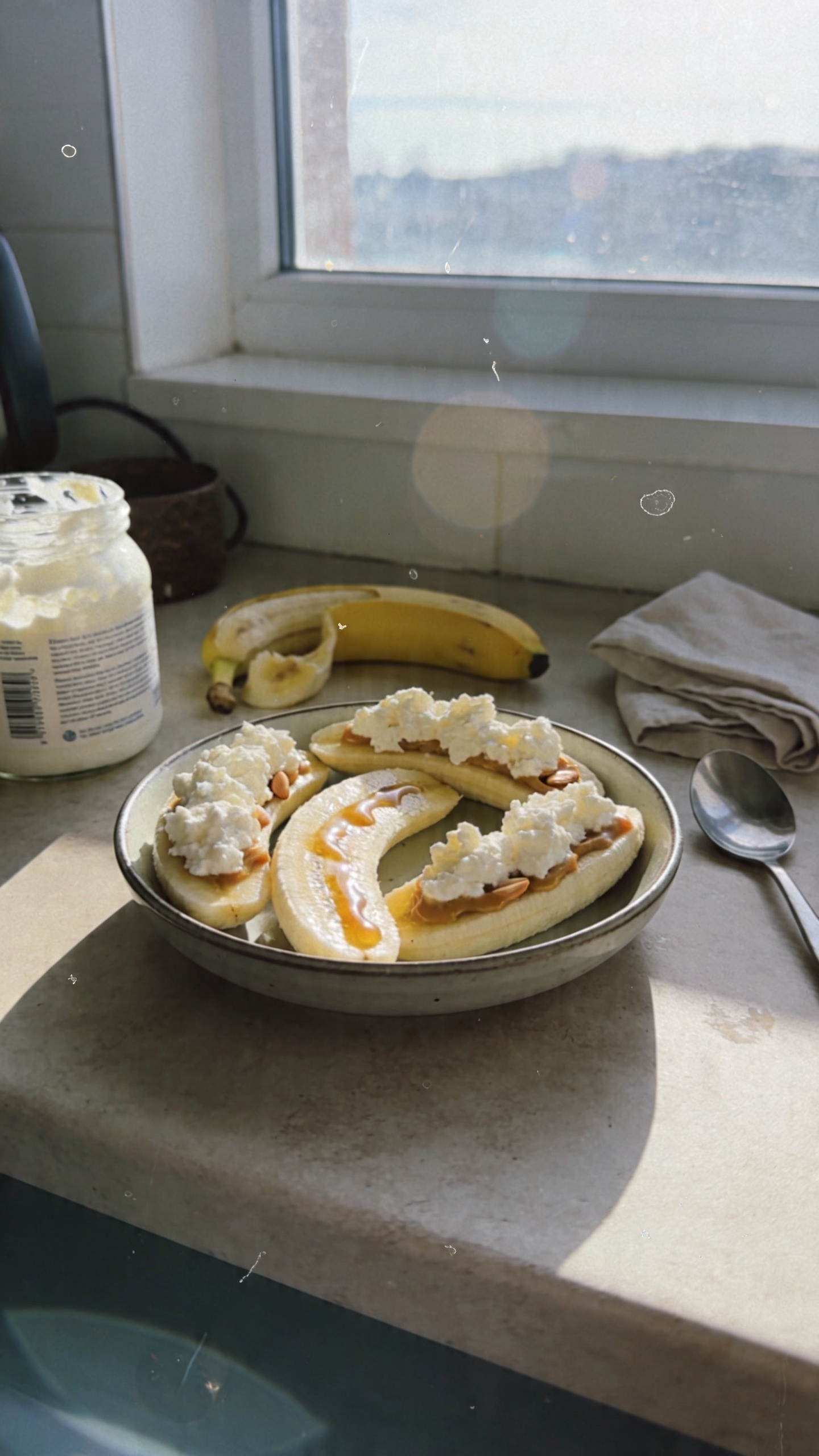 A candid, real-looking photo of creamy cottage cheese banana boats as the main subject, taken in a home kitchen or breakfast nook with natural window light. The scene shows ripe banana halves topped with fluffy cottage cheese, optional drizzle of honey or almond butter, arranged casually on a small plate or in a simple bowl. Include everyday breakfast clutter: a jar of cottage cheese, a partially used banana, a spoon, a loosely folded napkin, and a countertop with warm, natural tones. The shot should feel un-staged and like it was taken quickly with an iPhone: slight overexposed highlights on the glossy banana skin, a small lens flare from the window, minor motion blur from a quick handheld angle, and a subtle grain that varies with light. The horizon may tilt slightly and there should be a faint fingerprint smudge or smudged lens effect for realism. Colors are natural and slightly muted, no heavy retouching, no text overlays. The overall vibe is a casual, everyday breakfast moment captured in 1080p-like quality, conveying a simple, energy-boosting snack without perfection. Optional post-processing hint: subtle, natural-looking adjustments that resemble “scaled down and up again” with light sharpening and a flat, non-studio color tone. No words on the image.