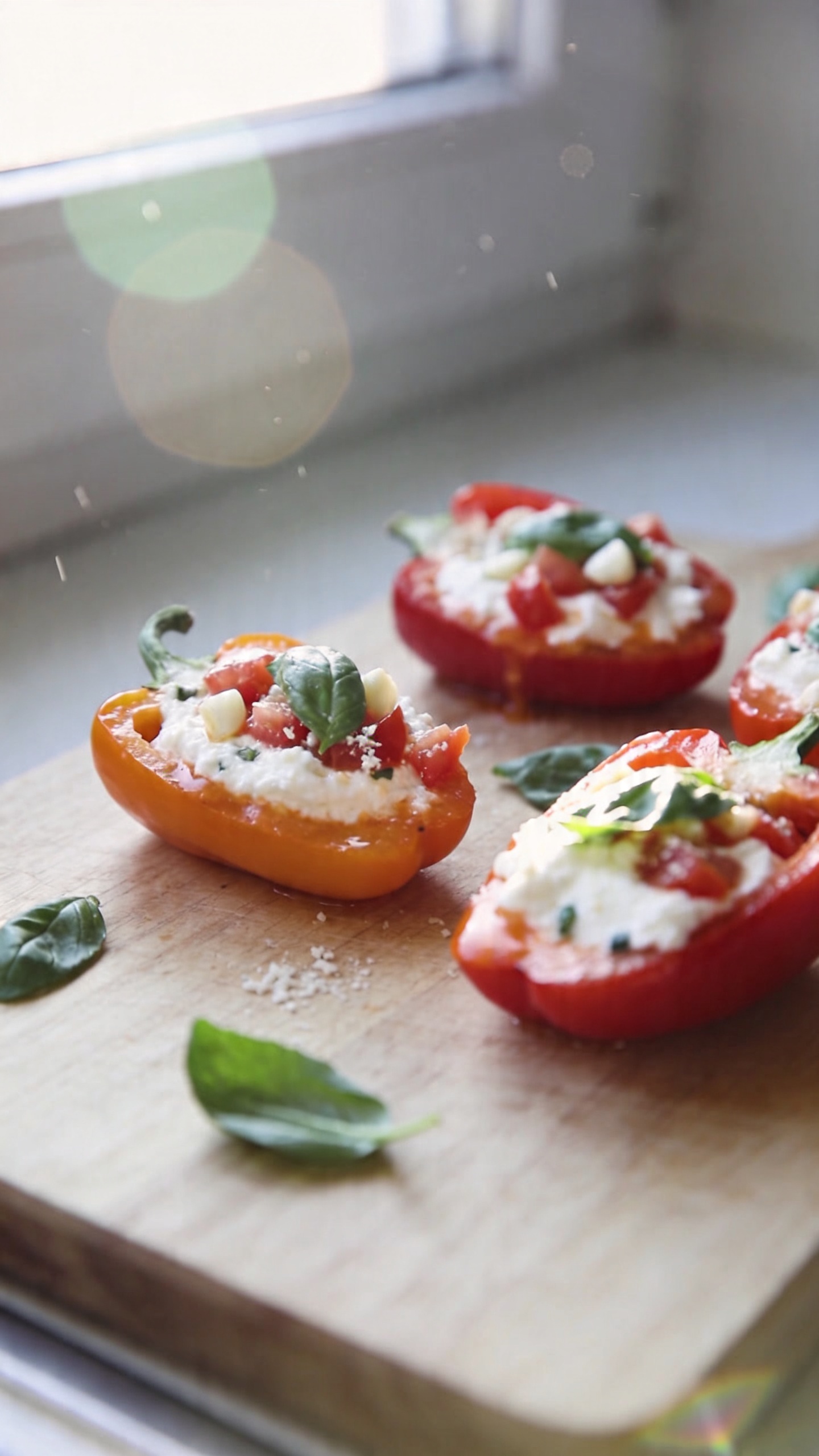 An everyday kitchen scene featuring spicy tomato basil cottage cheese stuffed peppers as the main subject, captured in genuine, unpolished iPhone photo style. A casually plated half-up, half-down view of halved mini bell peppers filled with a creamy cottage cheese mixture (with visible chopped tomatoes, garlic, and fresh basil) resting on a simple wooden cutting board. Bright, natural window light streaming in from the side, slightly overexposed highlights on the glossy pepper skins, subtle lens flare, and a few stray basil leaves for realism. The scene should feel real and unscripted: a quick, in-the-moment shot taken in a hurry, no staging. Include minor imperfections: slight motion blur from a quick hand movement, a touch of grain in the lighter areas, a slightly tilted horizon, and a tiny fingerprint or smudge on the lens. The pepper fillings should look warm and inviting, with a light tomato sauce sheen and a small sprinkle of parmesan just barely visible. Composition is casual and imperfect, resembling a real, everyday meal photo captured with an iPhone in natural kitchen lighting—no text, no cinematic or studio effects, roughly 1080p quality with a realistic, unpolished finish. Optional subtle hint of post-processing to suggest a quick edit (e.g., slight desaturation and minor sharpness tweak) but nothing that makes it look artificial. No words or branding in the image.