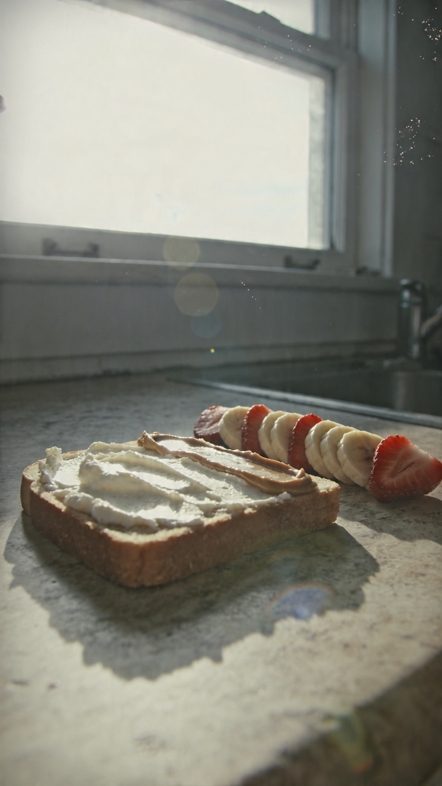 A candid, real-photo style of a Crunchy Nut-Butter Bond breakfast on a rustic kitchen counter: a slice of toast with cottage cheese spread, a thin streak of almond or peanut butter, and neatly arranged fruit slices (banana and strawberry) on top, all photographed in natural window light. The scene should feel unposed and everyday—no staging—with a casual, slightly imperfect composition. Include subtle iPhone-like imperfections: gentle overexposed highlights from the window, a small lens flare near the edge, a hint of motion blur from a quick grab, and grain that varies with the light. The horizon may be slightly tilted, and there could be a fingerprint smudge on the lens in the corner. The image should look compressed, 1080p quality, as if taken quickly on an iPhone in a busy morning routine. No text, no branding, no cinematic or studio cues. Optional subtle post-processing hints: a tiny, natural-looking bump in contrast that resembles a quick, imperfect edit, but keep it looking authentic and not overly polished. Shot quickly, no staging, no AI-like perfection.