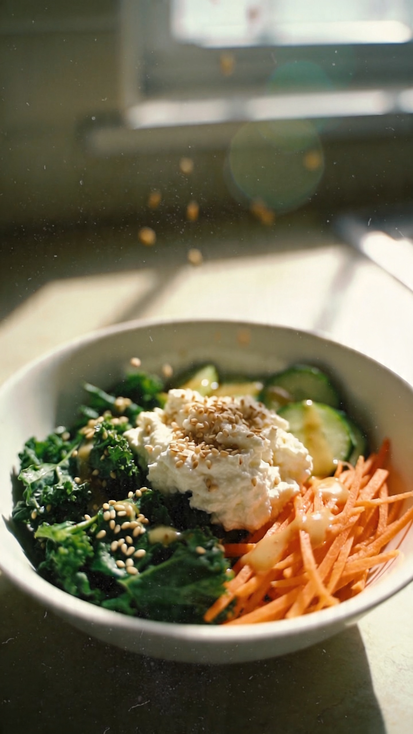 A real, authentic iPhone photo of a cozy kitchen scene featuring a Umami Sesame Greens Bowl as the main subject, with earthy greens and sesame-scented cottage cheese on a simple white bowl. Include 1 cup cottage cheese, baby spinach or kale, sesame seeds, shredded carrots and cucumber, and a light soy drizzle visible. Casual, imperfect composition: a slightly tilted camera angle, natural window light streaming in, soft shadows, and a warm, homey countertop background. Subtle, realistic camera imperfections: slight overexposed highlights from the window, minor lens flare, gentle motion blur from a moment of reaching for ingredients, grain varying with light, fingerprint or dust specks on the lens. The scene should feel everyday and unscripted, as if shot quickly in a real kitchen with no staging. No text, no words on the image. Compressed, 1080p quality with a hint of post-processing that looks like a quick edit (subtle color tweak, slight smart blur with a touch of sharpening) but not obviously artificial. Optional: hint that greens rotate for variety, keeping the bowl looking fresh and simple.