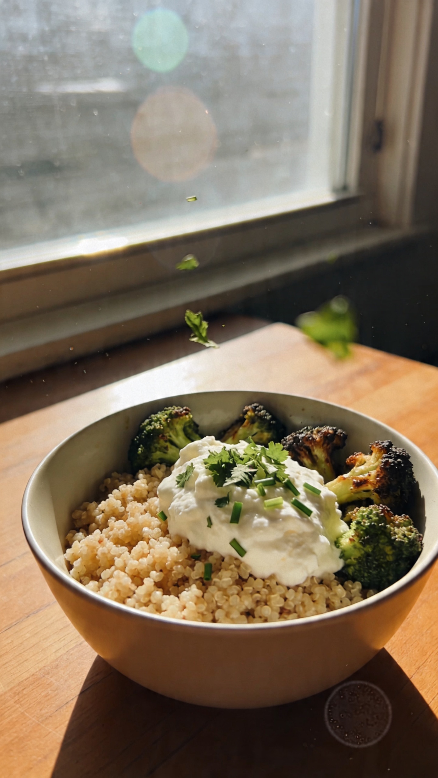 A real, authentic photo of a cottage cheese quinoa crunch bowl inspired by the heading "15. Herbed Quinoa Crunch Bowl." Shot casually as if captured on an iPhone by a home cook: half a cup of fluffy quinoa, topped with a generous scoop of cottage cheese, sprinkled with chopped parsley and chives, and roasted broccoli florets around the edge. The bowl sits on a wooden table near a window with natural light streaming in, a slightly tilted horizon, and a candid, imperfect vibe. Include natural camera imperfections: a few slight overexposed highlights from the window, gentle lens flare, tiny motion blur on a leafy herb piece, subtle grain in the shadows, and a minor fingerprint or smudge on the lens. Composition appears unstyled and unposed, as if “taken in a hurry,” with no staging. The image should feel like “compressed, 1080p quality” with a casual, everyday look—no text, no cinematic or studio terms; keep it realistic, warm, and approachable. Optional subtle post-processing hints: a tiny bit of smart blur and sharpening, but nothing polished or overly polished to hint at AI generation. No words or overlays.